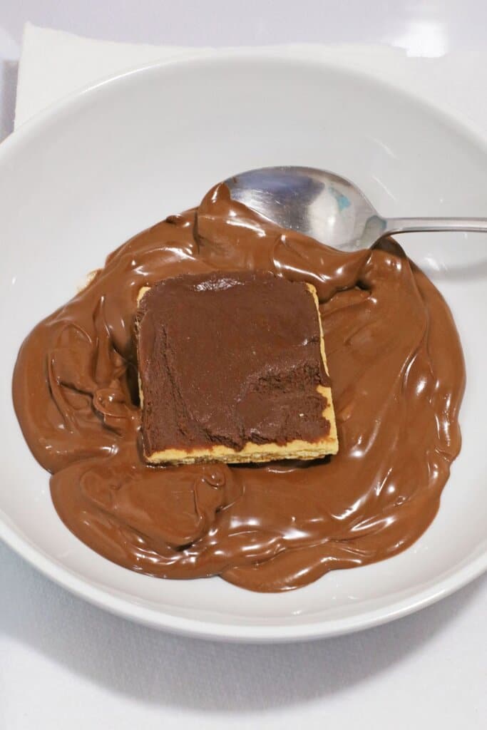 Graham crackers being dipped in melted chocolate.