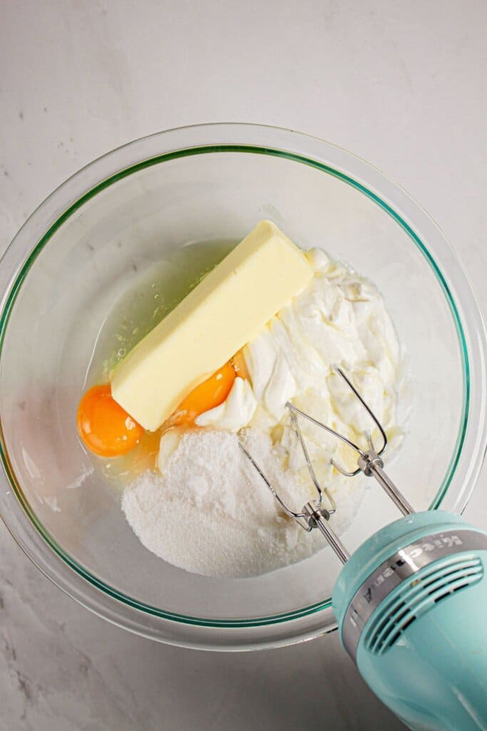 Butter, sour cream, and eggs being mixed together in a glass mixing bowl.