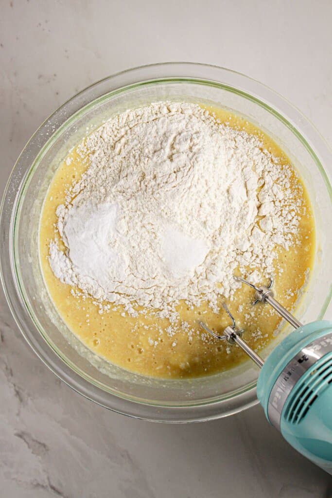 Dry ingredients being added to wet batter in a glass mixing bowl.