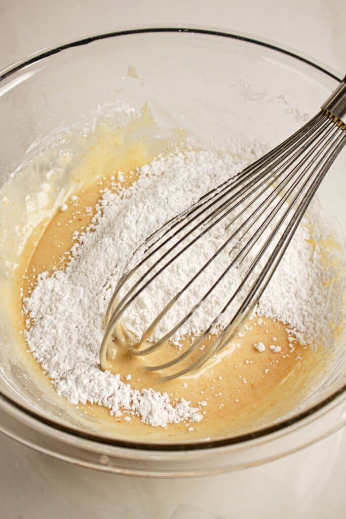 Browned butter and powdered sugar being mixed together in a glass bowl.