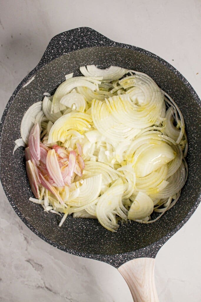 Onions and shallots being cooked in a skillet.