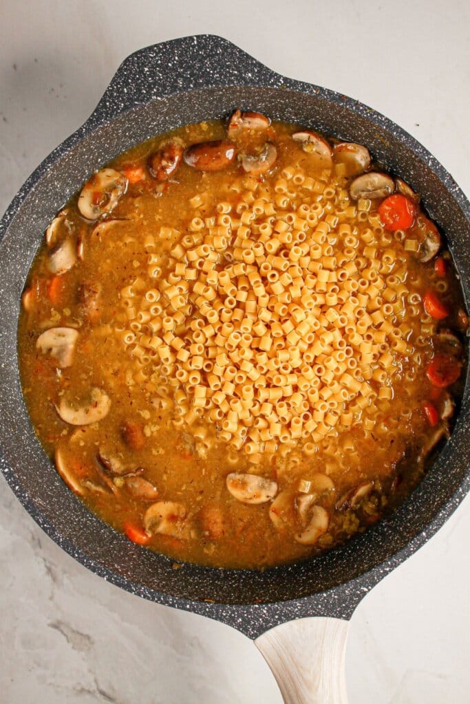 Ditalini noodles being added to a large skillet.