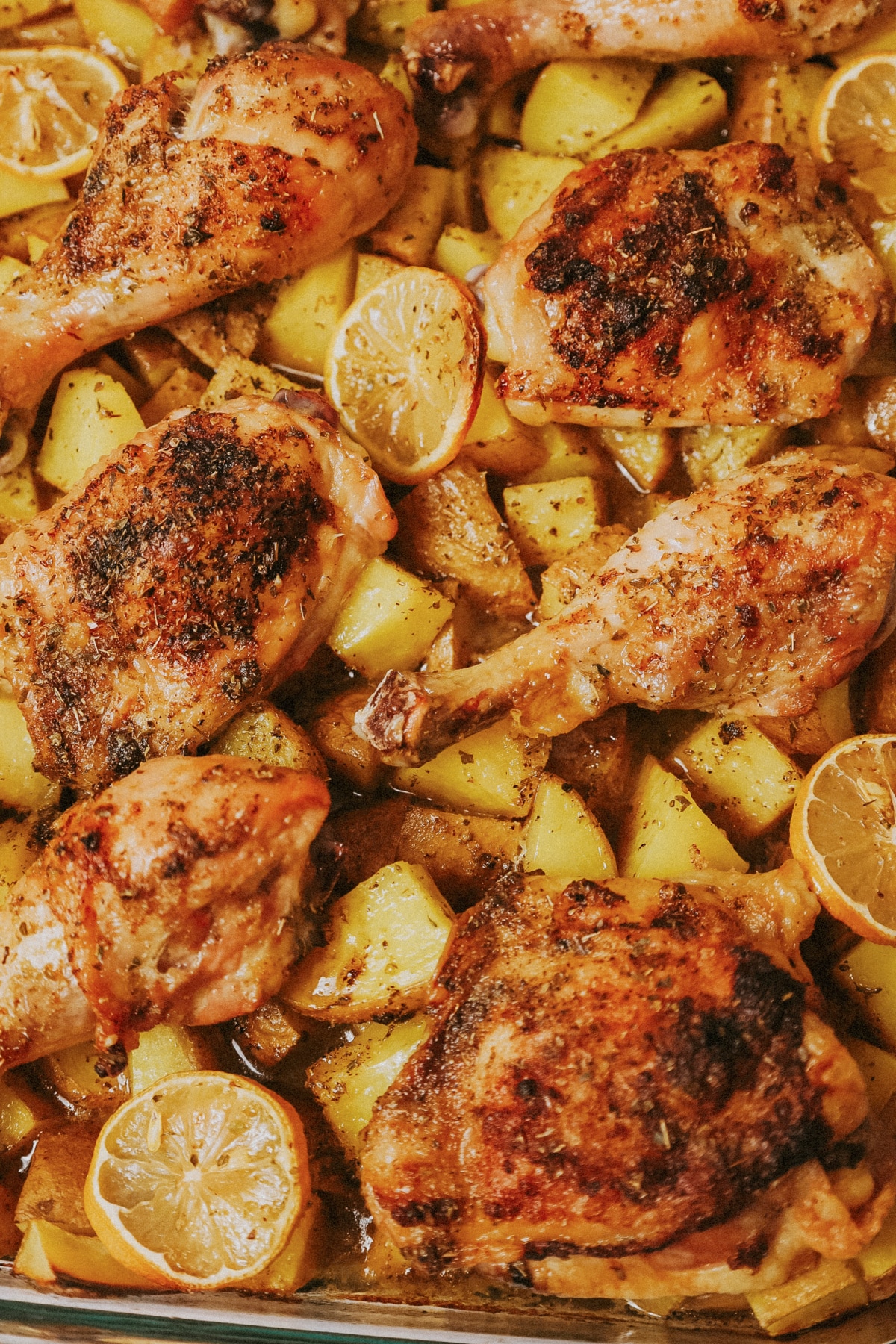 Glass baking dish full of chicken pieces and potatoes.
