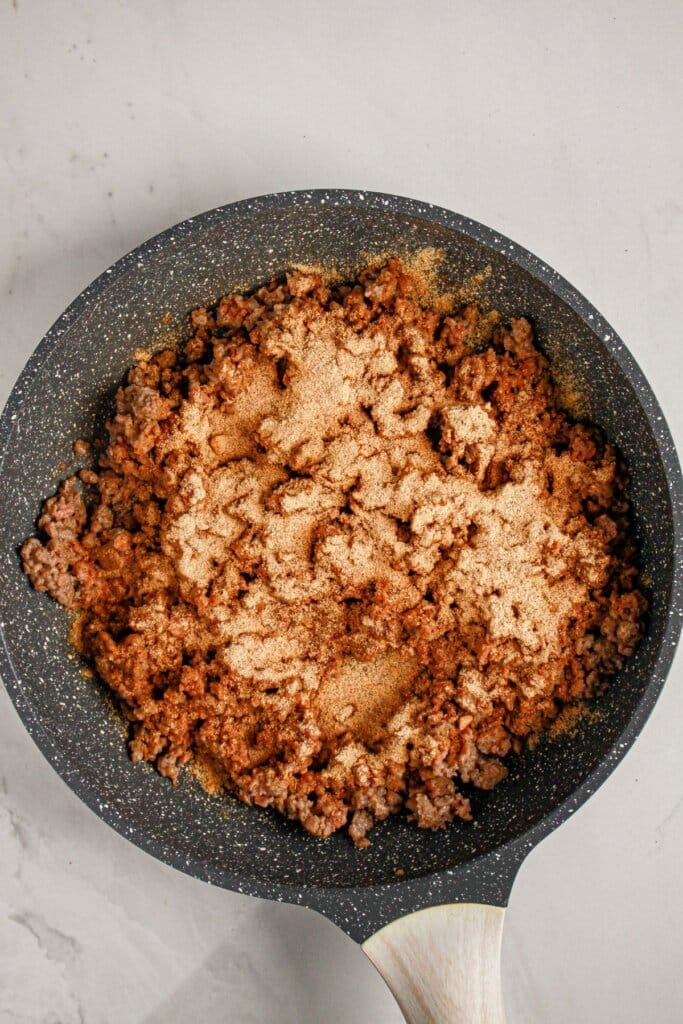 Ground beef being cooked and seasoned in a skillet.