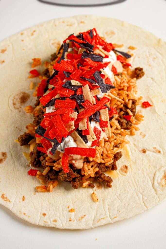 Tortilla strips being added to the top of beef and rice.