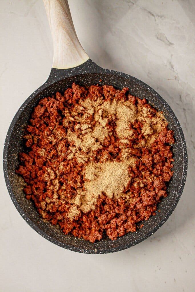 Ground beef being cooked and seasoned with taco seasoning in a skillet.