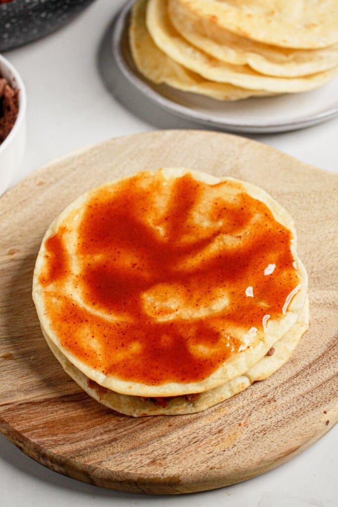 Sauce being spread on top of a tortilla.