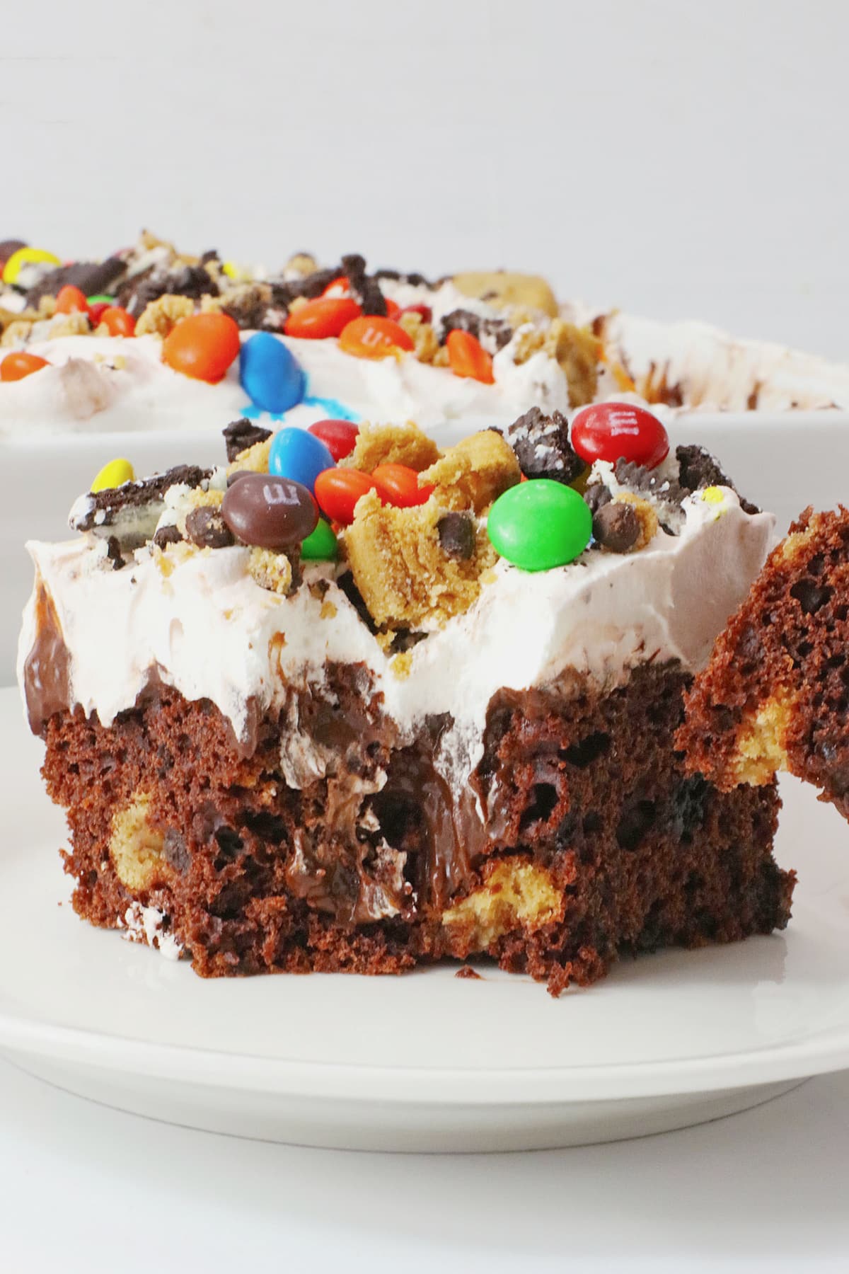Slice of monster cookie poke cake on a white plate.