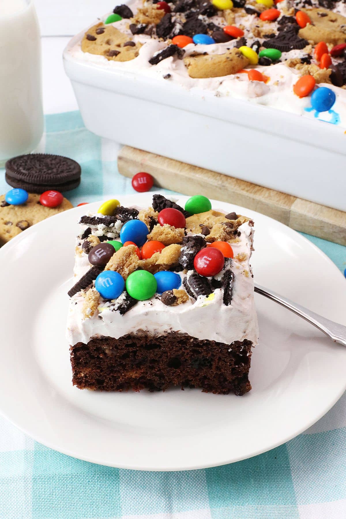 Slice of monster cookie poke cake on a white plate.