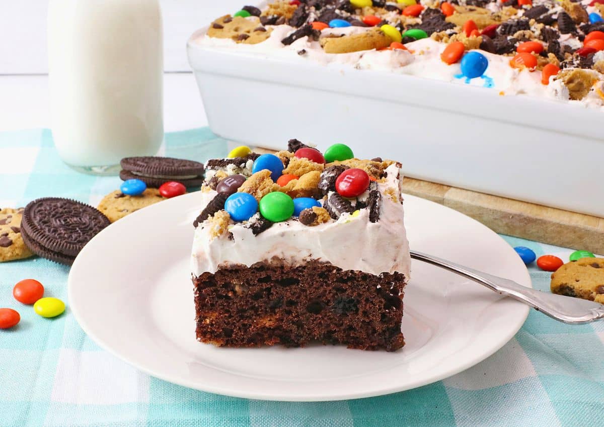 Slice of monster cookie poke cake on a white plate.