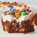 Slice of monster cookie poke cake on a white plate.