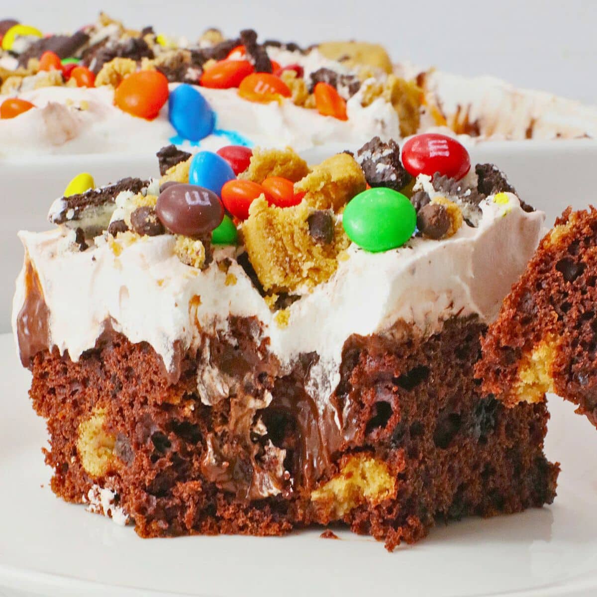 Slice of monster cookie poke cake on a white plate.