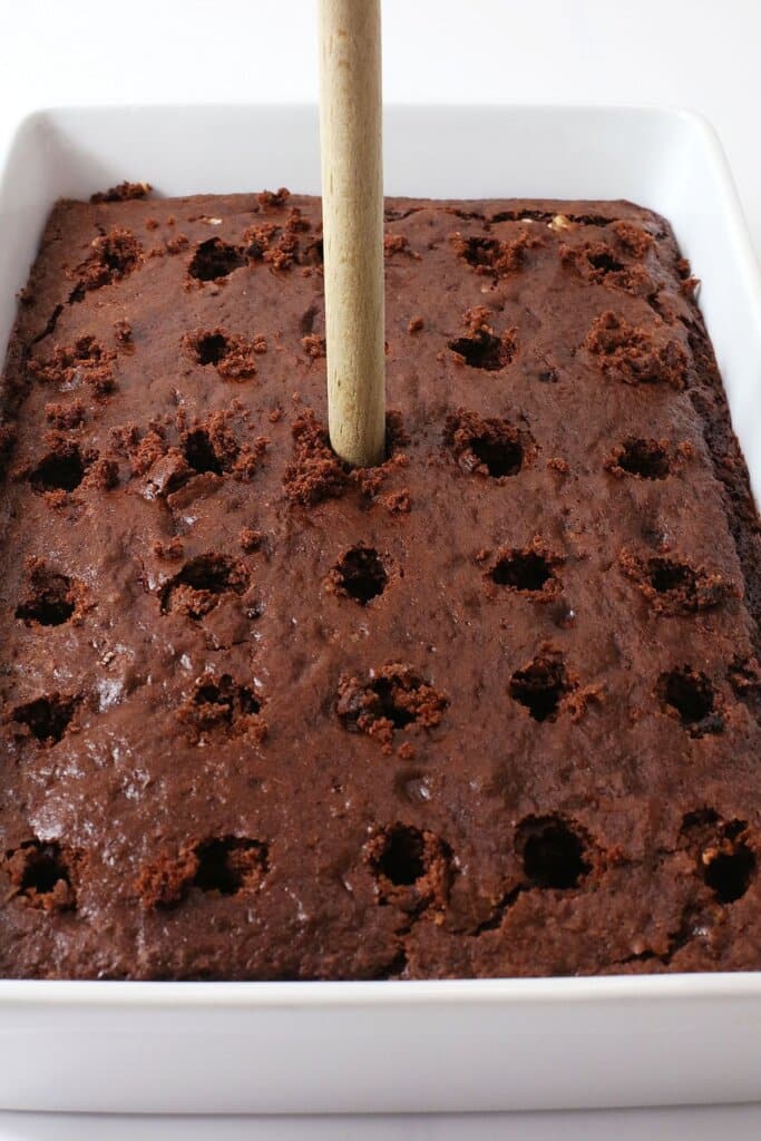 Holes being poked into chocolate cake with a wooden spoon.