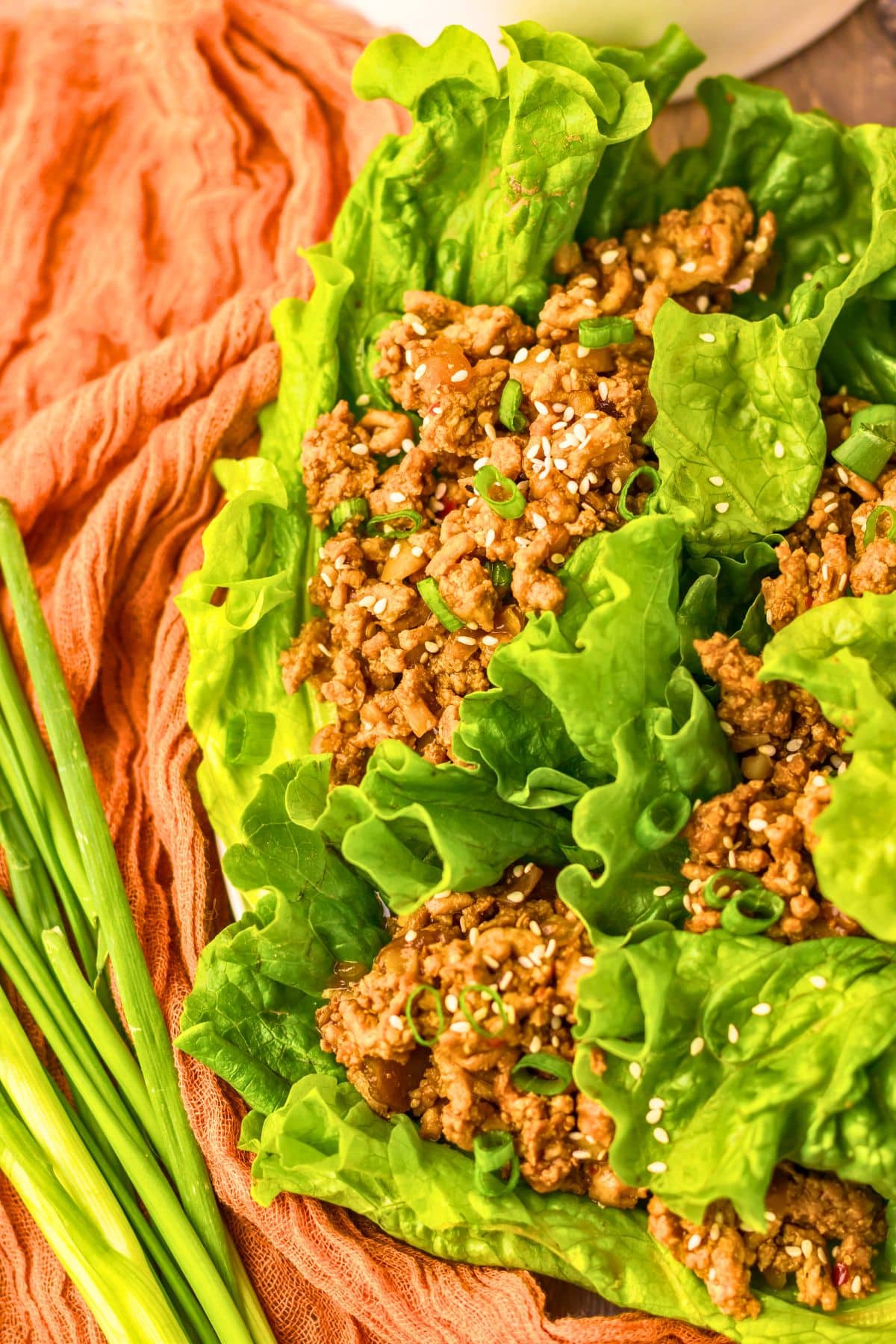 Lettuce cups filled with chicken on a white plate.