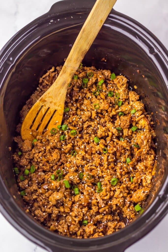 Cooked meat topped with green onions in a slow cooker.