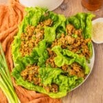 Lettuce cups filled with chicken on a white plate.