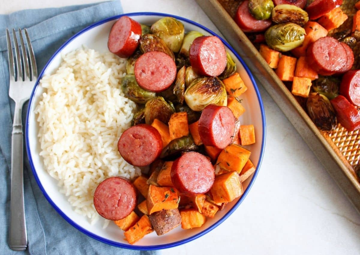 White plate full of sausage, veggies, and rice.