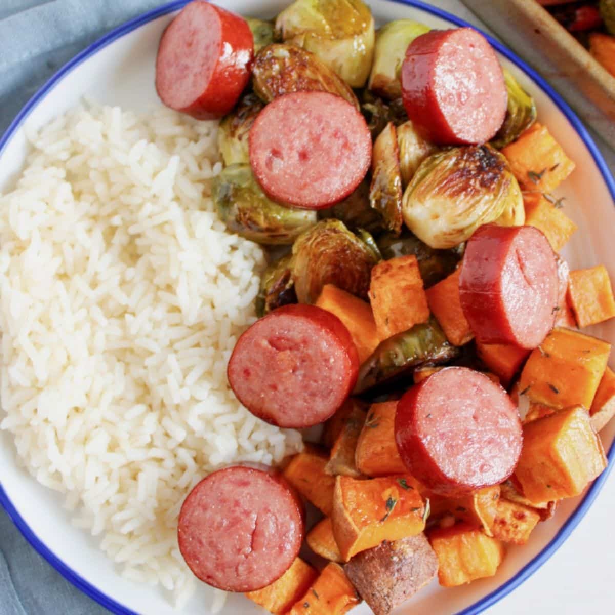 White plate full of sausage, veggies, and rice.