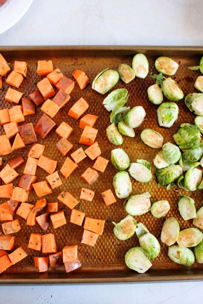 Sweet potatoes and brussels sprouts on a baking sheet.