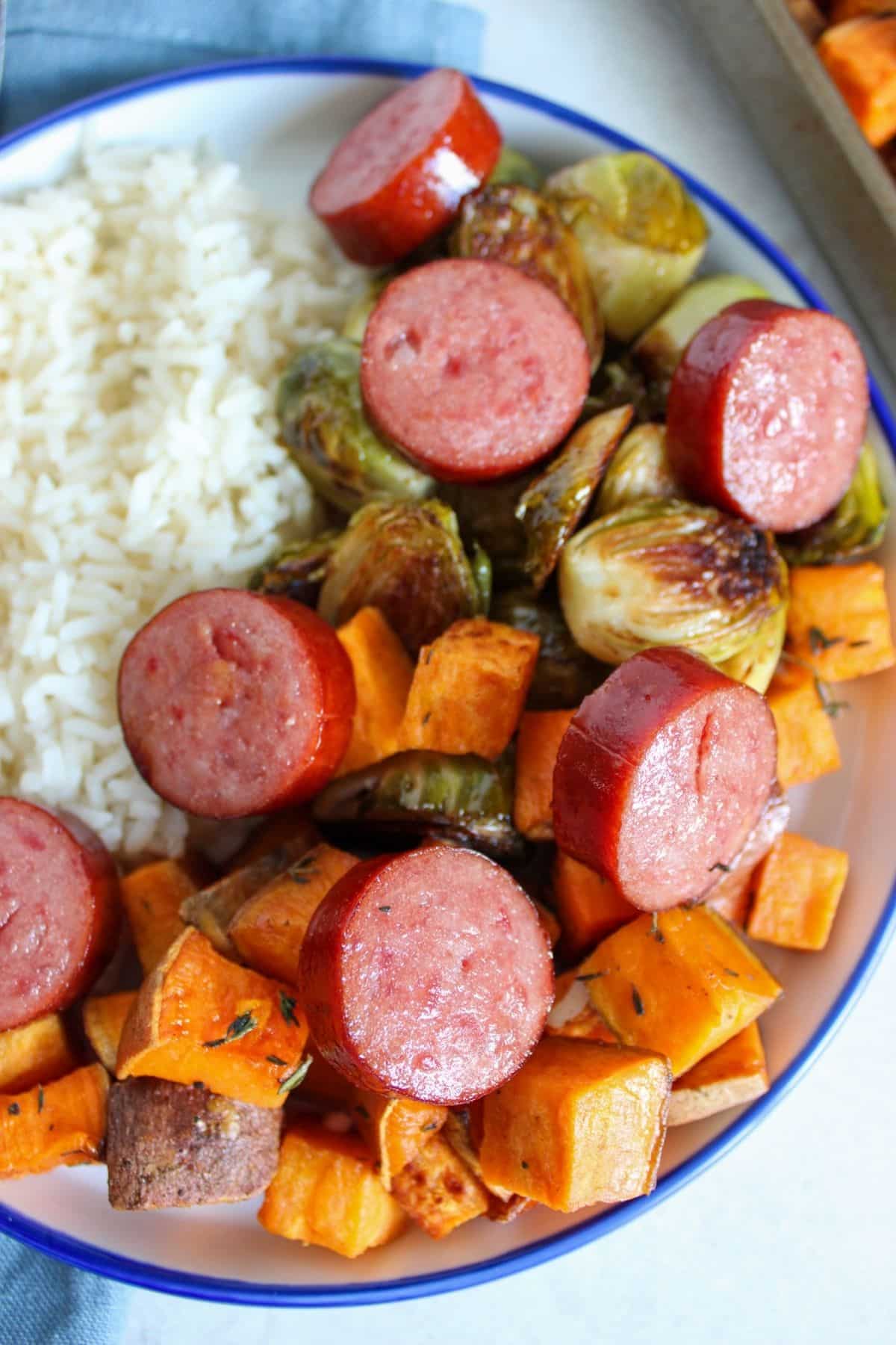 White plate full of sausage, veggies, and rice.