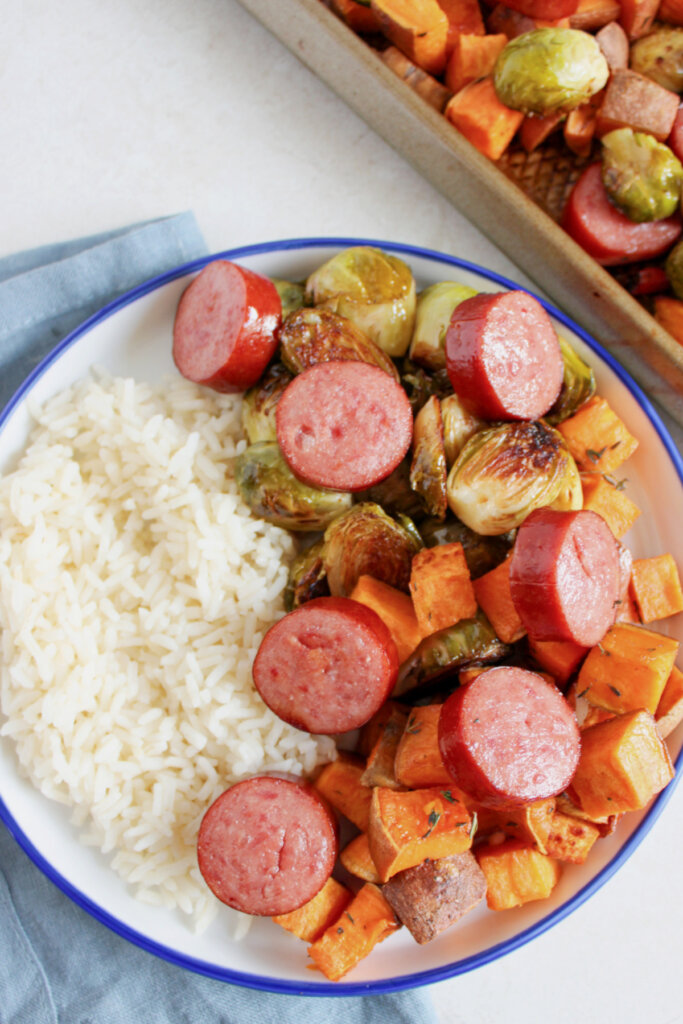 White plate full of sausage, veggies, and rice.