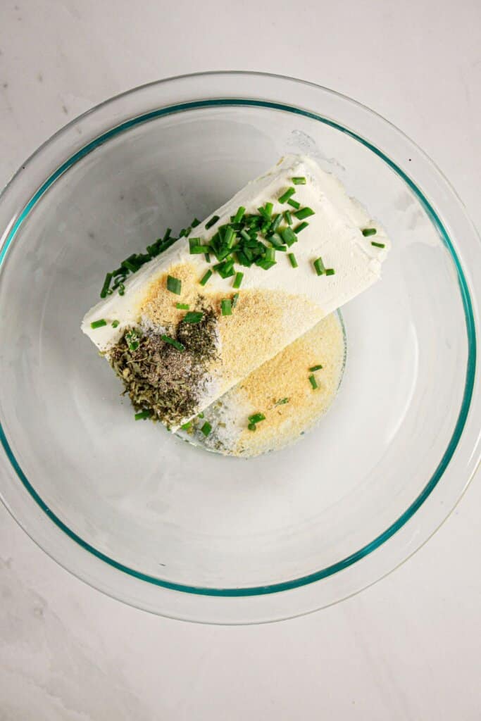 Cheese and seasonings being mixed together in a glass mixing bowl.