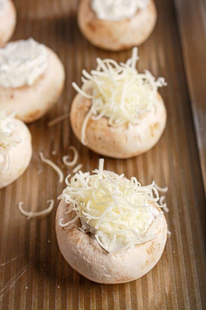 Parmesan cheese being sprinkled on top of caps on a baking dish.