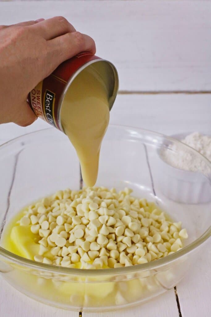 Condensed milk being poured on top of white chocolate chips.