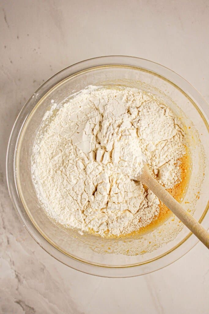 Dry ingredients being added to dough in a glass bowl.
