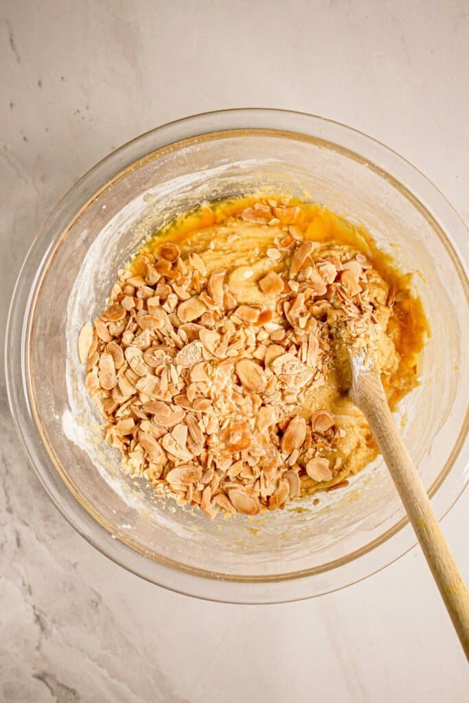 Almonds being stirred into dough in a glass bowl.