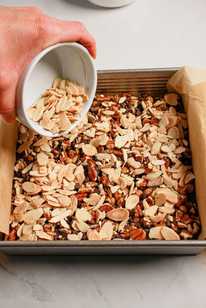 Sliced almonds being sprinkled on top of dessert in a baking dish.