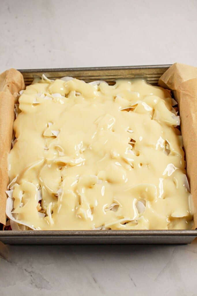 Condensed milk being poured on top of dessert in a baking dish.