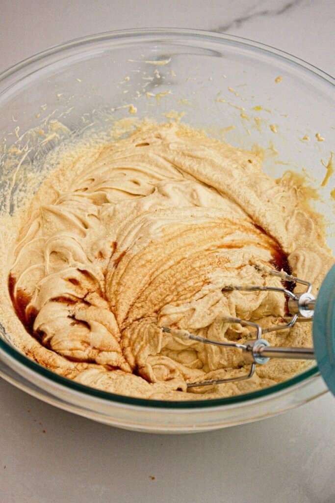 Batter being mixed in a large glass bowl with a hand mixer.