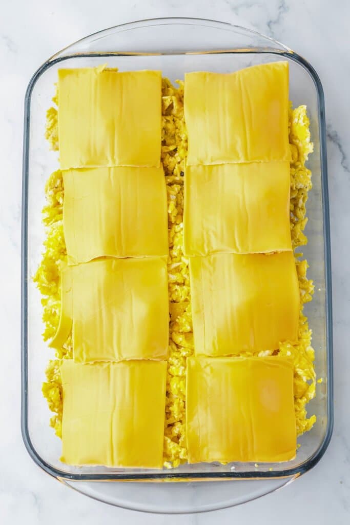 Eggs and cheese on top of sandwiches in a baking dish.