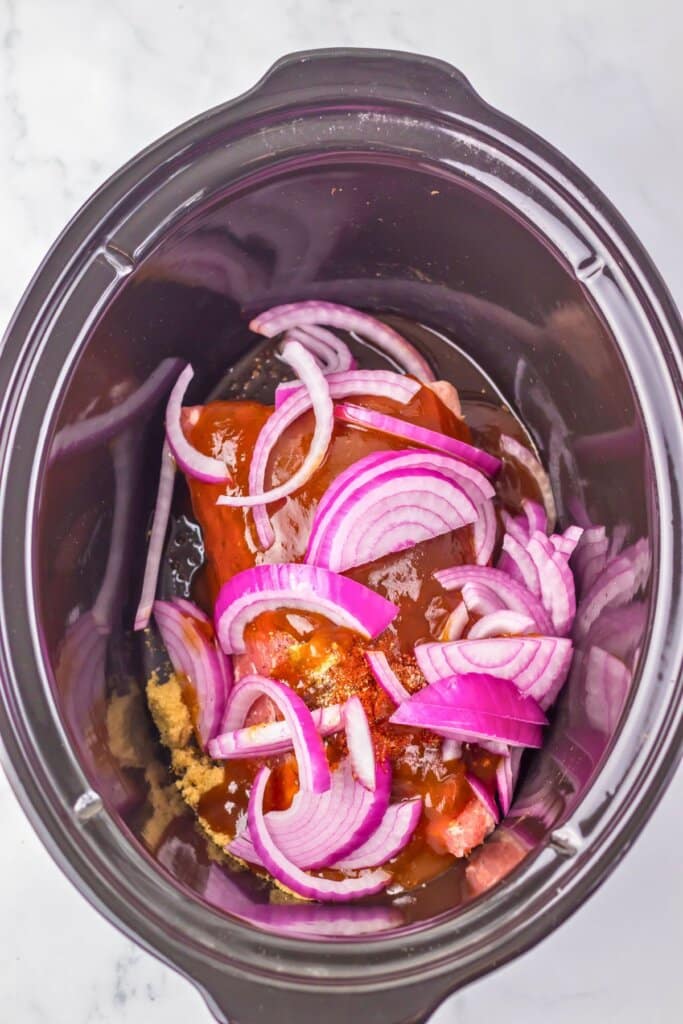 Red onions, brown sugar, meat, and sauce in a crock pot.