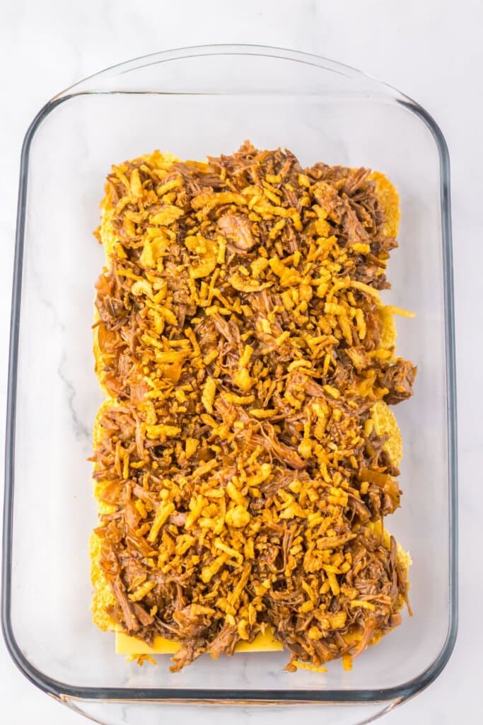 Meat and onions being sprinkled on top of rolls.
