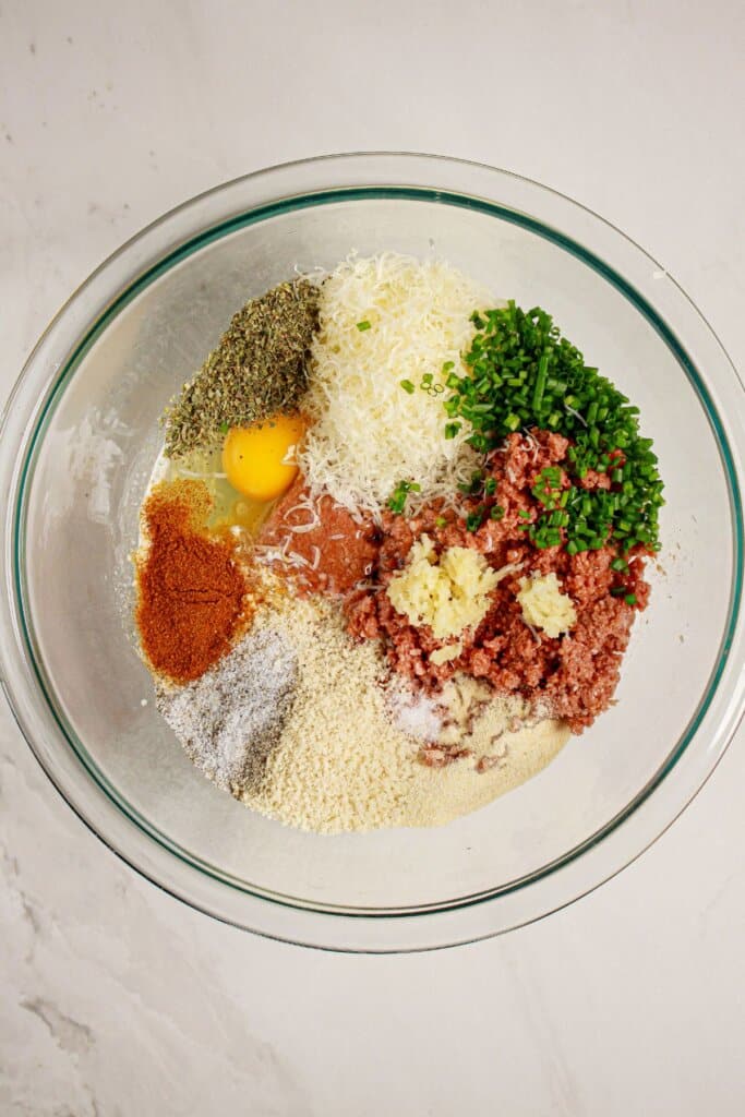 Beef, spices, breadcrumbs, and egg in a glass bowl.