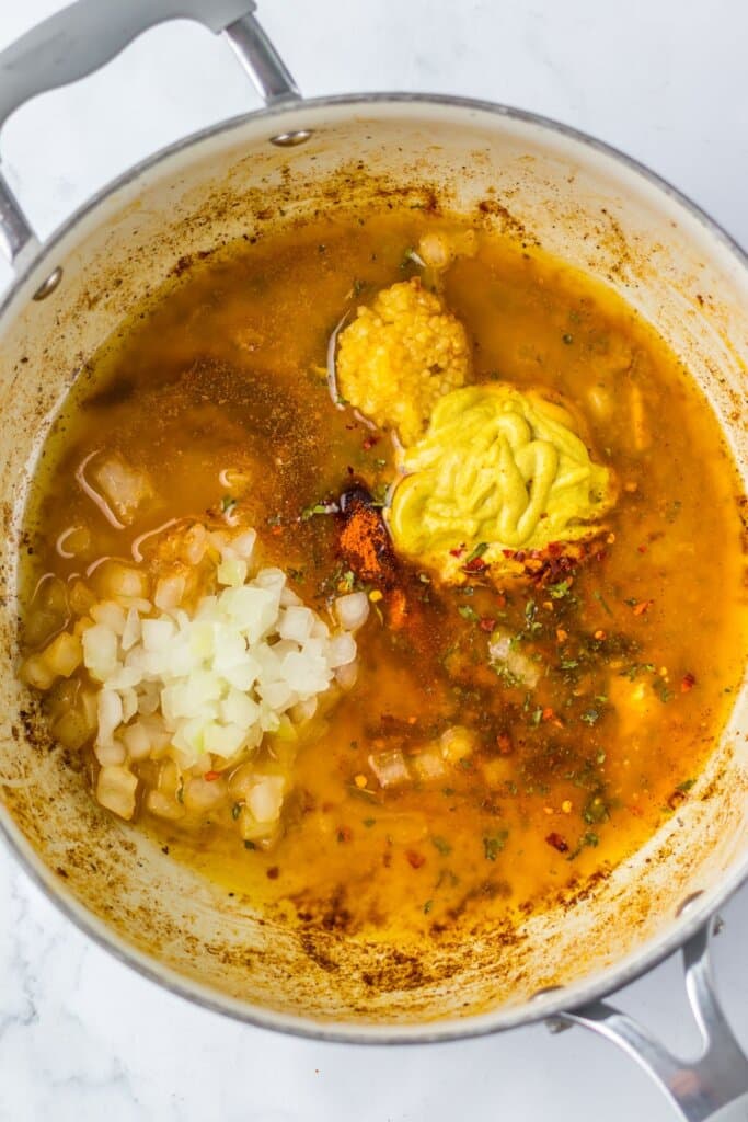 Onions, mustard, garlic, and seasonings in a pot.