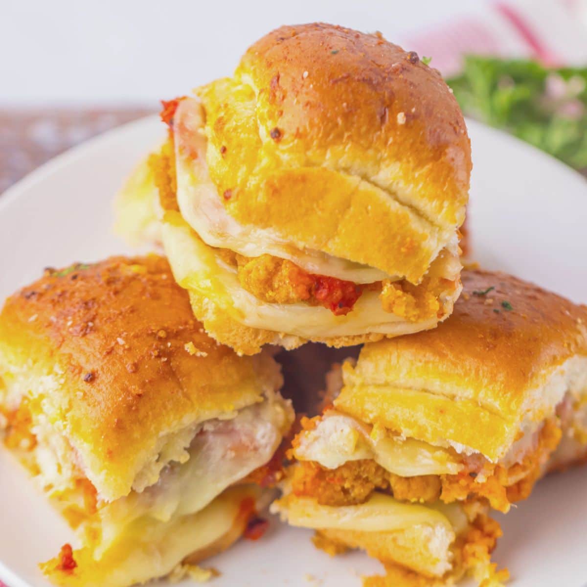 Three chicken parmesan sliders stacked on a plate.