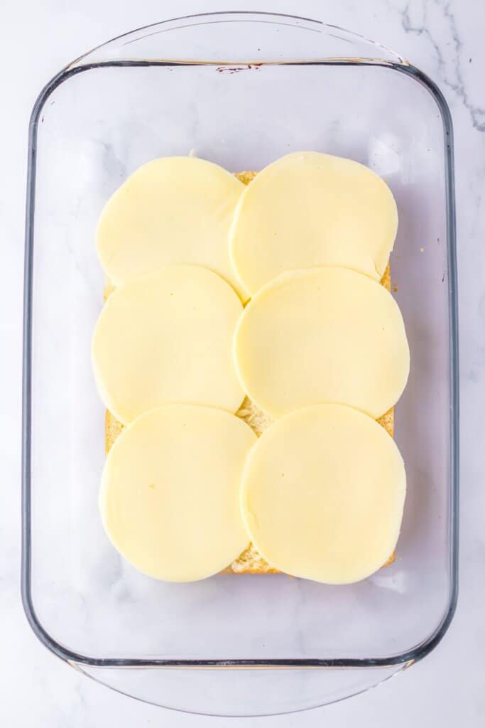 Slices of cheese being layed on top of rolls.