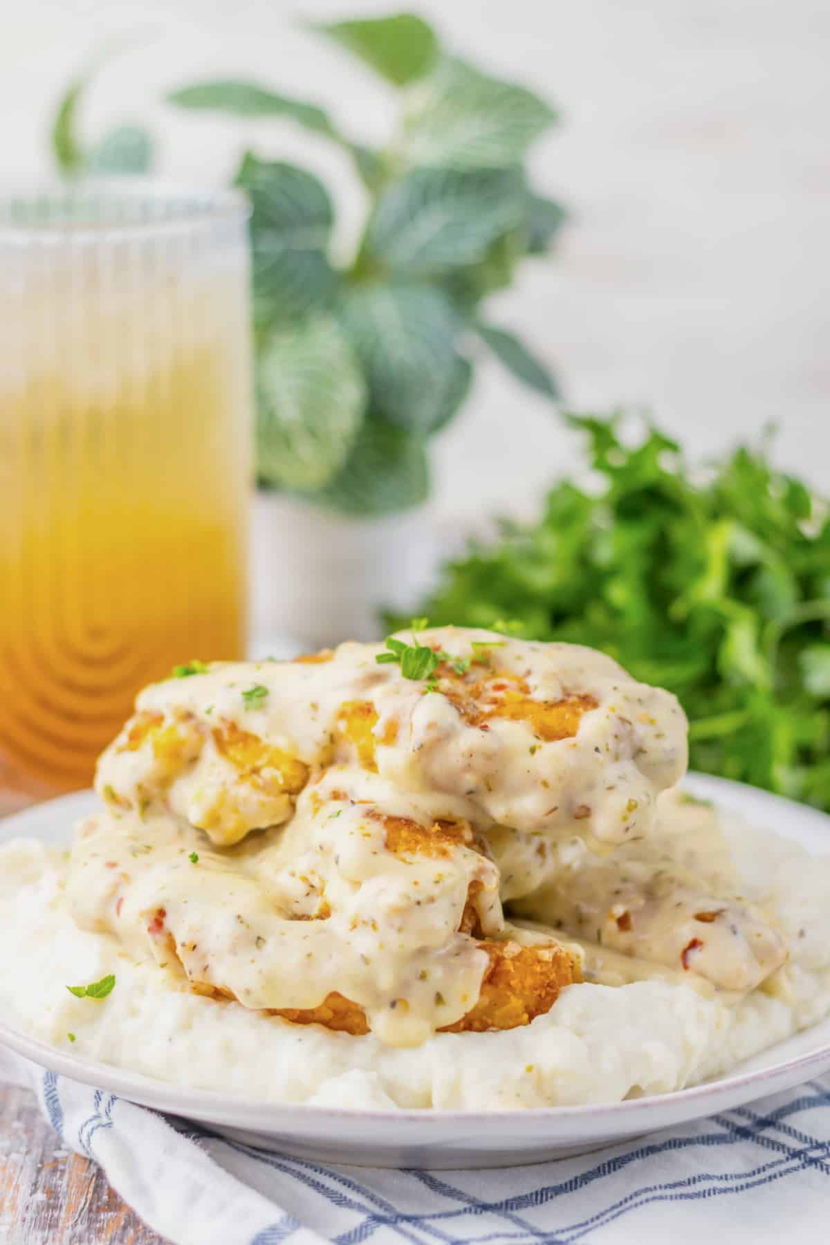 Garlic parmesan chicken tenders on a bed of mashed potatoes on a white plate.