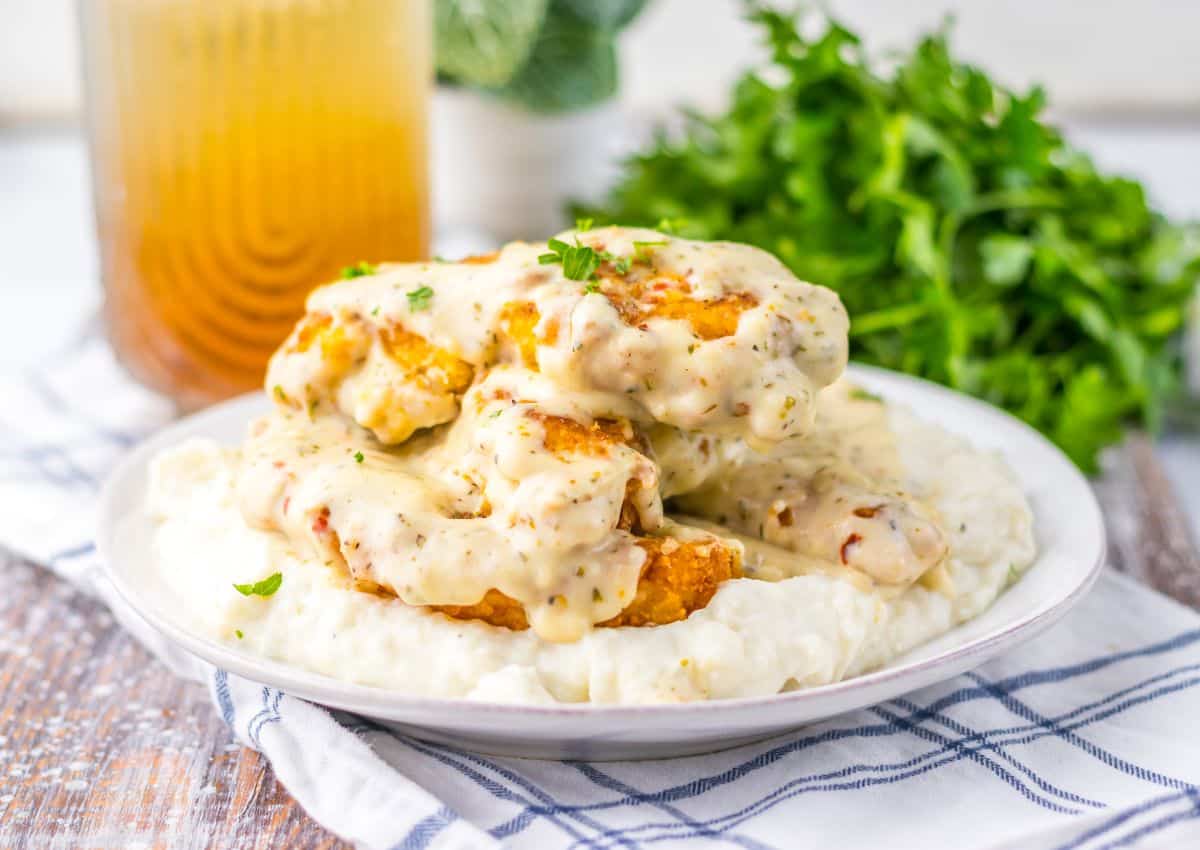 Garlic parmesan chicken tenders on a bed of mashed potatoes on a white plate.