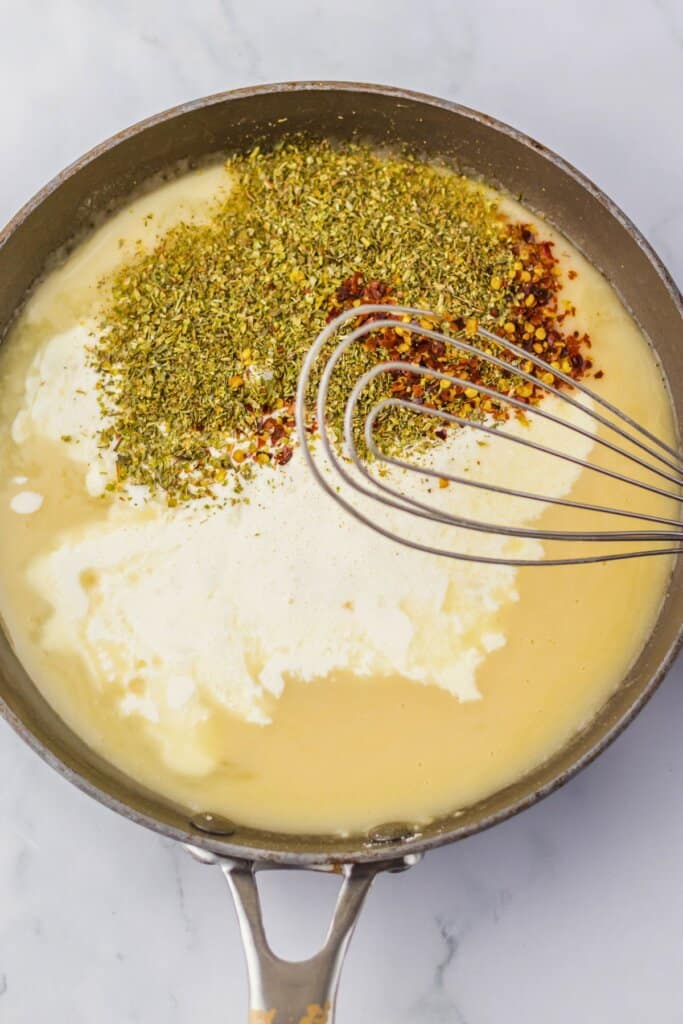 Seasonings being added to sauce in a large skillet.