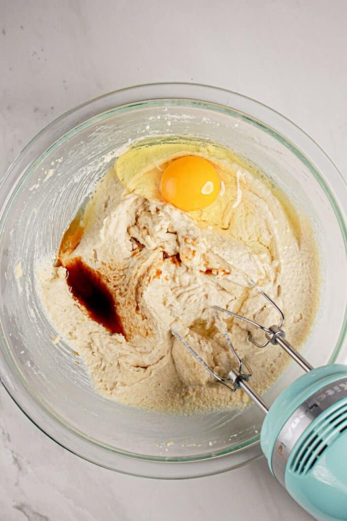 Egg and vanilla being added to batter in a glass mixing bowl.