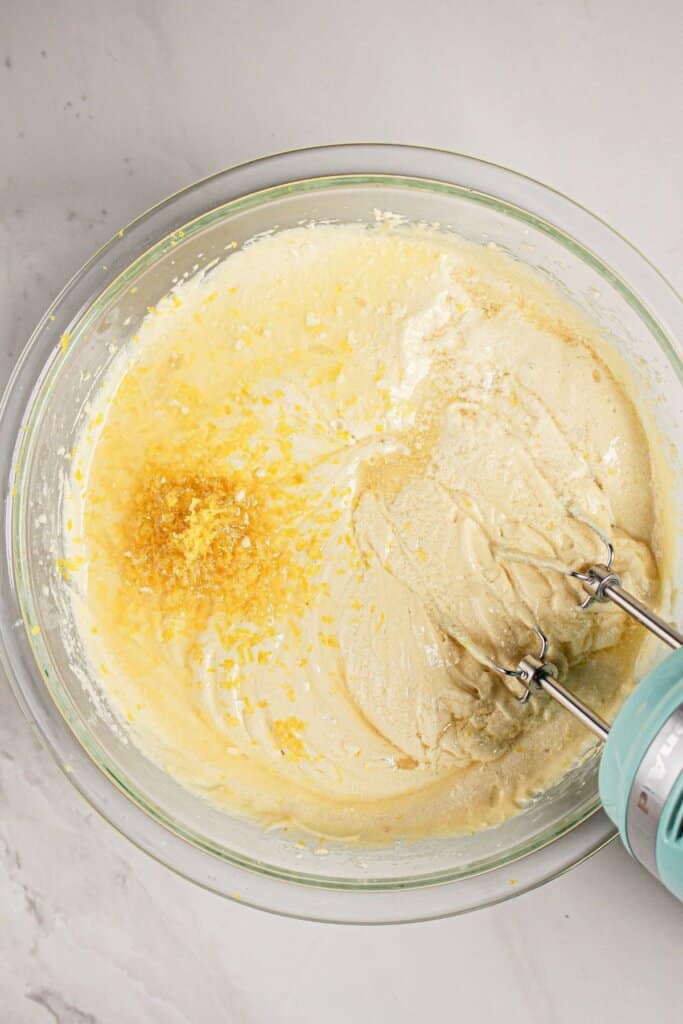 Lemon juice and lemon juice being added to batter in a glass bowl.