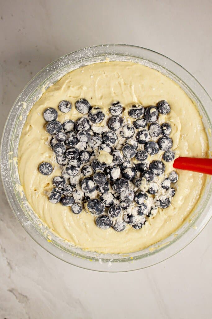 Blueberries being mixed into cake batter in a glass bowl.
