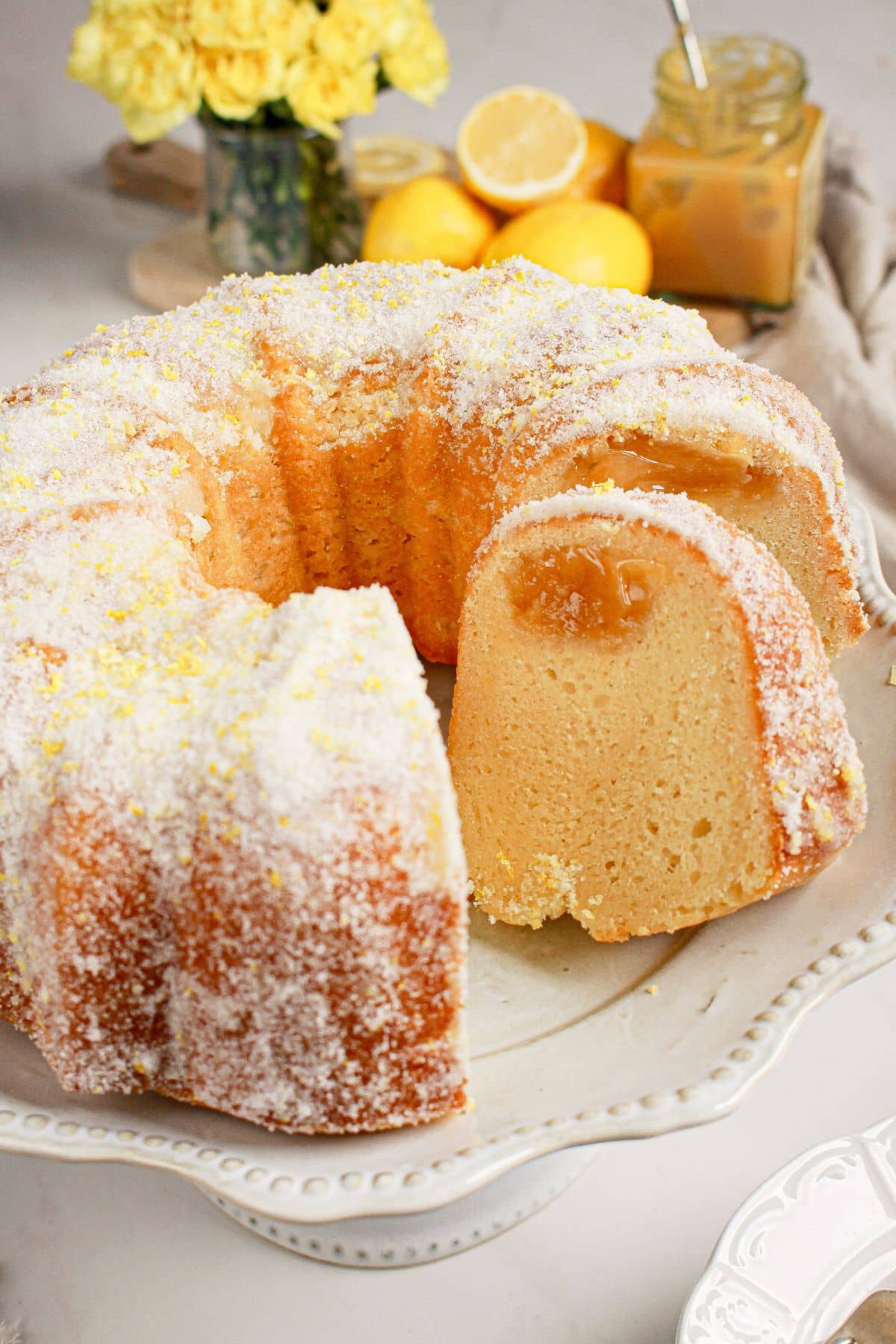 Lemon curd bundt cake on a cake plate with a couple slices missing.