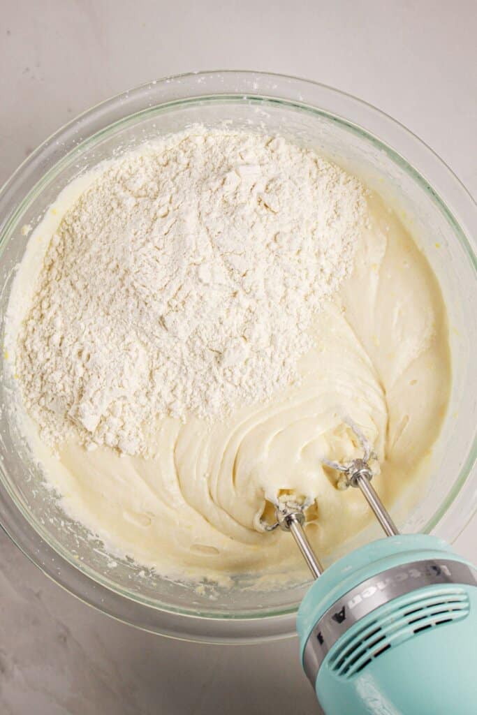 Dry ingredients being added to batter in a large glass mixing bowl.