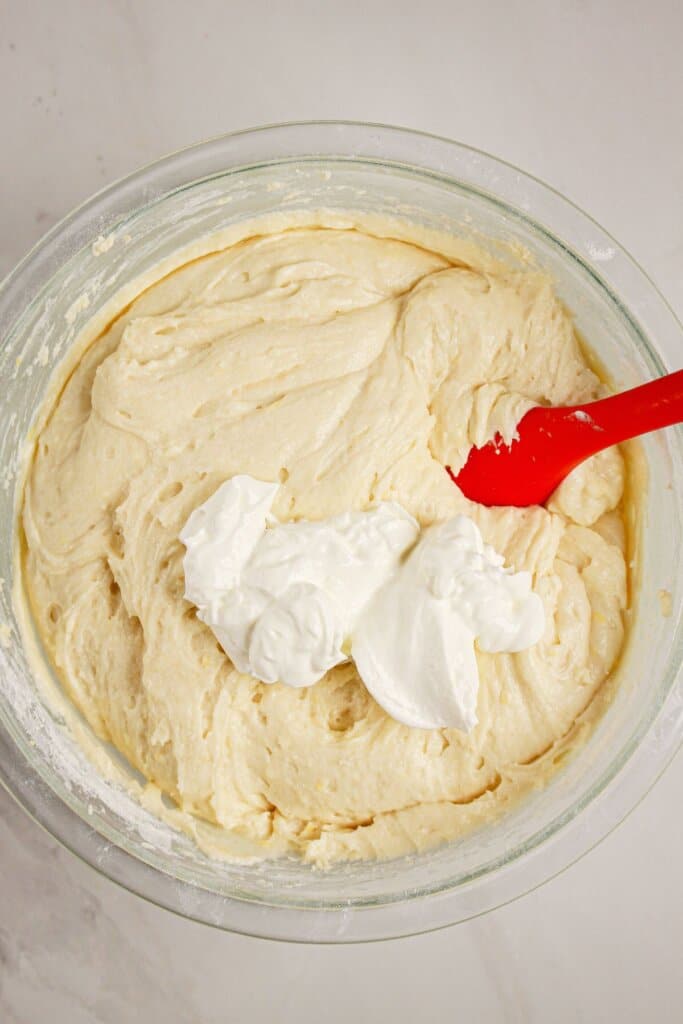 Sour cream being mixed into a batter in a glass mixing bowl.