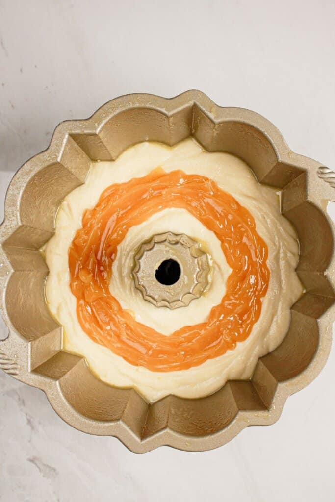 Lemon filling being swirled into batter in a bundt cake pan.